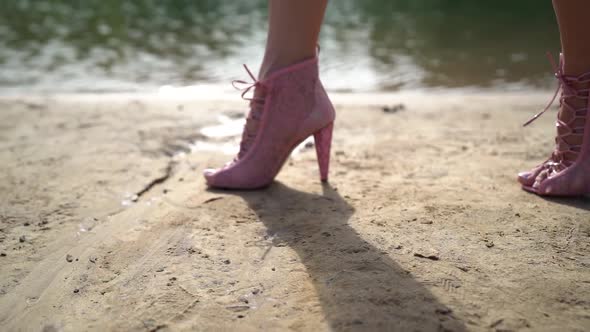 Woman Shod Pink Lace Shoes Is Walking Over Sand Coast of Lake or River at Sunny Day alt