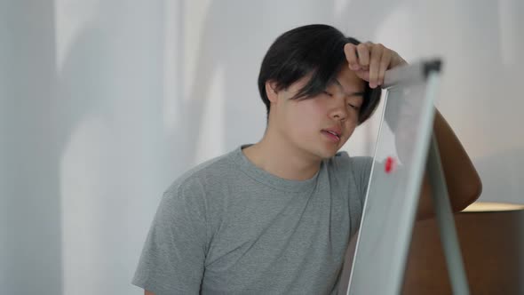 Portrait of Sad Exhausted Young Asian Man Leaning Head on Whiteboard Thinking alt