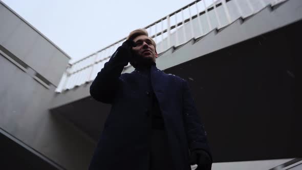 Young Businessman Speaks on Mobile Phone Near Business Center During Snowfall alt