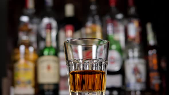 A Glass of Whiskey Slowly Rotates in the Bar an Ice Cube Falls Into the Glass alt