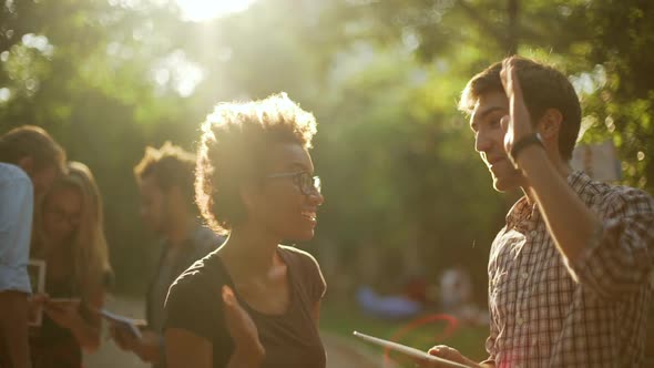 Joyful African American Female Giving High Five to Caucasian Male with Tablet in Park Witn Friends alt