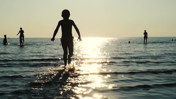 Little Girl Having Fun On Sea Shore. Kid Silhouette Running In The Sea.