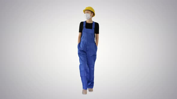 Young Woman in Yellow Hardhat and in Medical Mask Walking on Gradient Background. alt