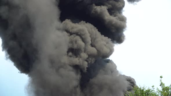 Black Smoke Rises Into the Sky. A Big Chemical Fire at a Factory Building. Thick Black Smoke Covers alt