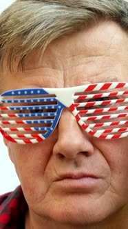 Serious Senior Mature Man Puts on Decorative Glasses in the Colors of the American Flag alt