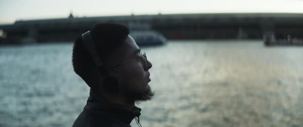 Profile view of a guy listening music next to the river and slowly dancing alt