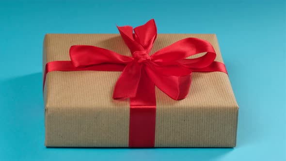 two female hands untie a red silk bow on the box, the gift is wrapped in brown kraft paper