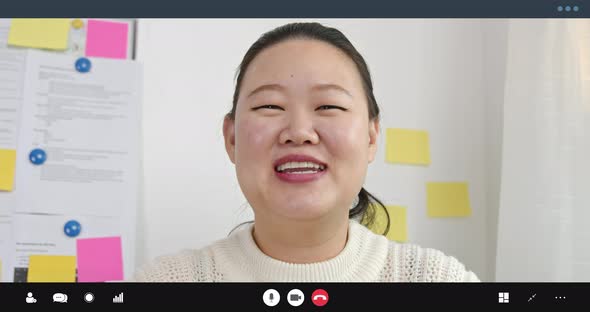 Young Asian woman smiling waving hand and talking on video call in office