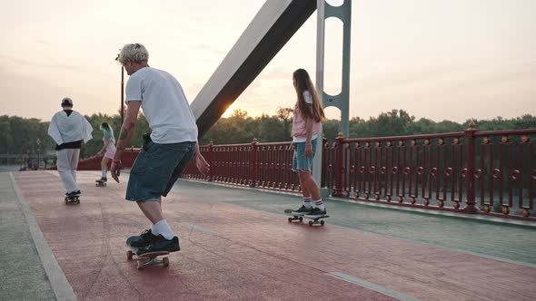 Group of Skaters Boys and Girls Ride Their Skateboards Across the Large City Bridge at Dawn alt