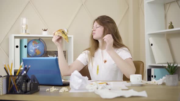 Young Woman Scratching Head and Eating Pizza As Sitting in Front of Laptop alt