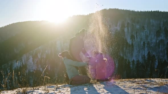 Young Parents Play Snowballs with Their Young Sons on the Top of the Mountain