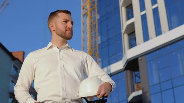 Architect Engineer in a White Shirt on the Background of a Modern Glass Building and Holding a alt