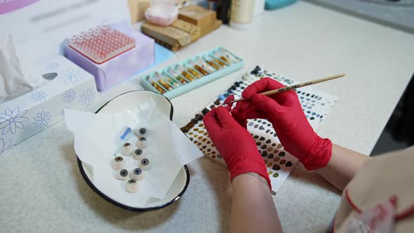 Hands in pink gloves holds plastic eye. Ocular prosthesis alt