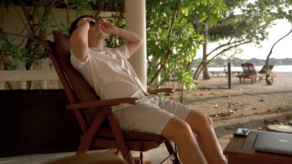 A Man Rests on a Chair on the Shores of the Indian Ocean Wearing Glasses alt