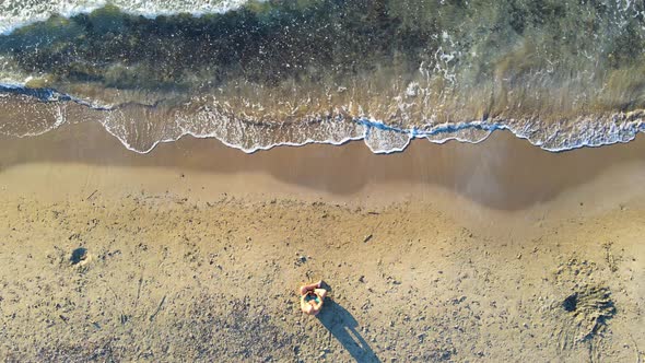 Aerial drone view of man sitting on the beach contemplating the sea alt