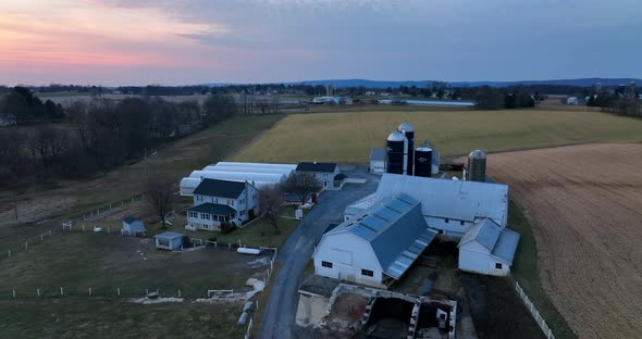 American farm with barn buildings, silo, greenhouse in winter pasture setting. Aerial pullback revea alt