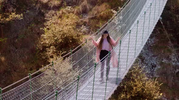 Young Woman Walks on Footbridge Over Yellowed Trees in Park alt