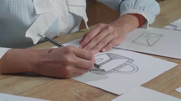 Close Up Of Woman Designer Sketching Hand Bag On The Layout Bond alt
