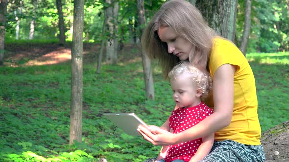 Woman With Cute Baby Girl Using Tablet Computer In Park