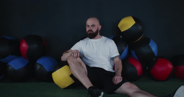 Portrait of Serious Young Bearded Caucasian Sportsman Sitting on Gym Floor Turn Head at Camera After alt