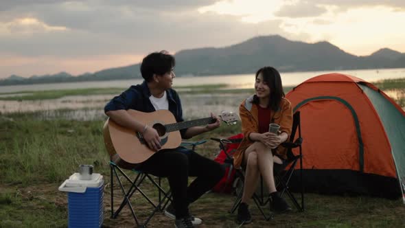 A happy young Asian couple backpacker playing the guitar and singing a song together.