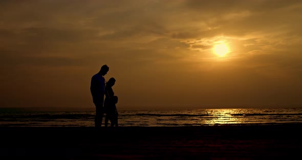 Silhouette of a Pregnant Woman with Her Husband and Child a Family Walking Along the Seashore at