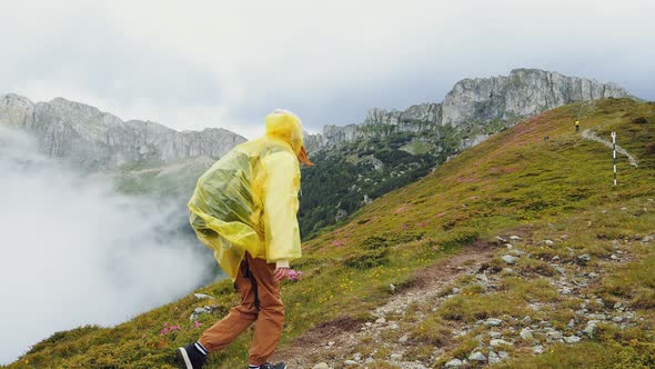 Woman in yellow rain coat going straightforward to the top of the mountain. alt