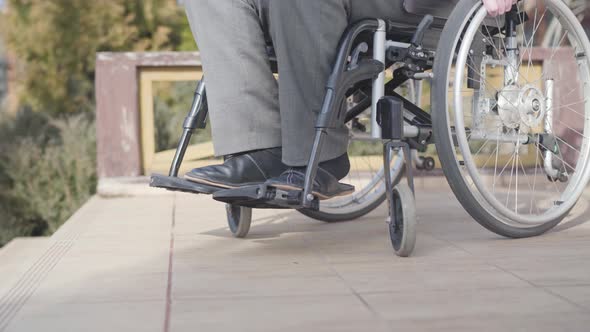 Side View Close-up of Wheelchair with Unrecognizable Old Man Rolling To Stairs. Concept of Ramp alt