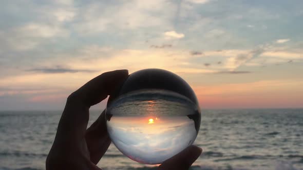 Hand holding crystal ball agains beautiful sunset over a sea