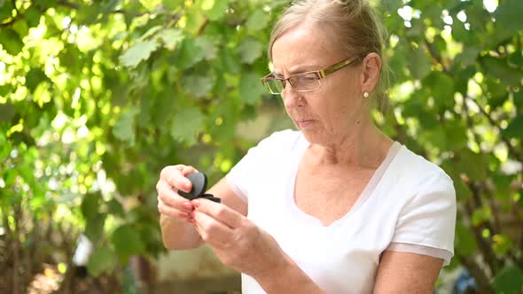 elderly excited senior woman learns how use the new wireless black headphones outdoor in the garden