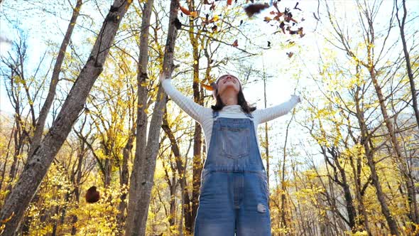 Happy Young Woman Having Fun and Throwing Yellow Leaves at Autumn Forest