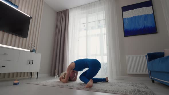 A Sporty Beautiful Woman Performs a Stand on Her Head and Hands at Home alt