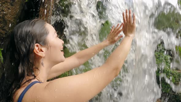 Beautiful Asian Girl Smiles Happily From Touching with Both Hands Powerful Waterfall Stream on