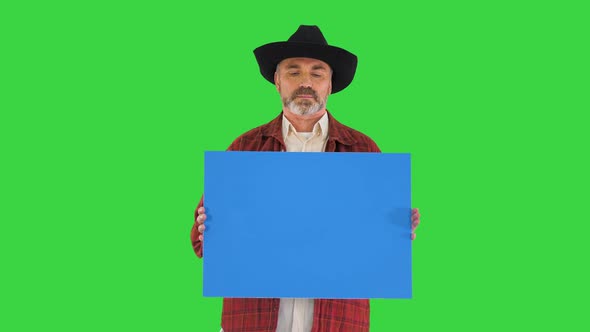 Serious Man in Cowboy Hat Looking To Camera and Holding Blank Placard on a Green Screen Chroma Key alt