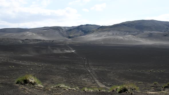White Car Driving Along Desert Area in Iceland Raising Dust in the Air