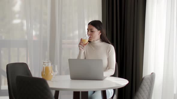 Young woman using a laptop computer and drinking healthy orange juice in the room