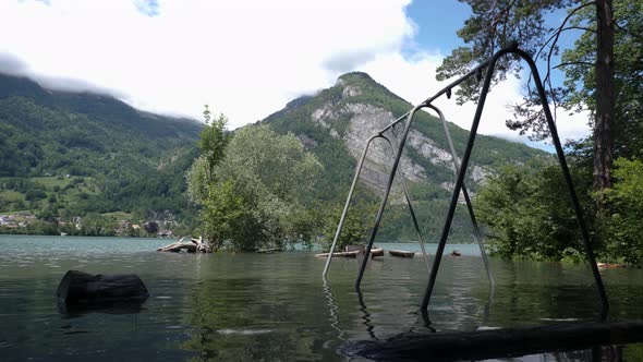 Playground with a swing in Switzerland is flooded and abandoned in front of a big mountain on a sunn alt