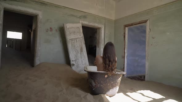 A Naked Young Woman in an Abandoned Building Sits with Her Back in the Bath Tub