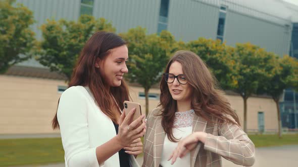 Happy Female Friends Browse the Contents of a Mobile Phone and Smile Sincerely, Two Twins Laughing alt