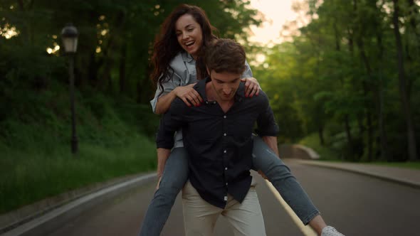 Young Man Piggyback Woman on Romantic Date in Summer Park at Sunset alt