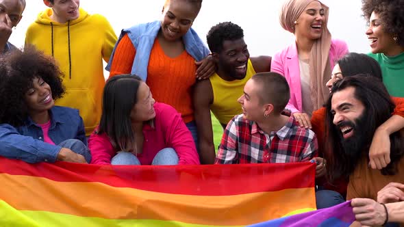 Group of multiracial people having fun at city park with rainbow flag - LGBT gay pride event