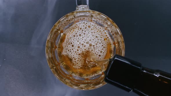 Top Close Up View of Beer Is Pouring From the Bottle Into Glass with Cold Smoke in Background