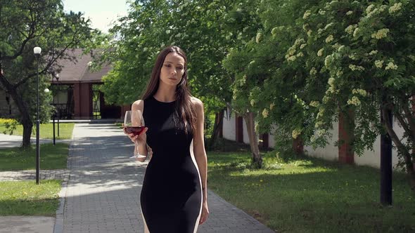 Elegant Woman with Glass of Wine Walking in Garden of Mansion alt