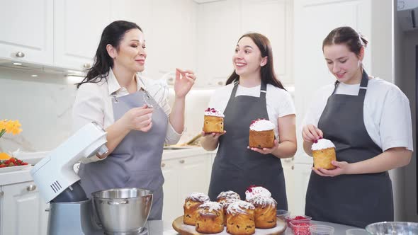 Women Taste Cream and Decorate Icing Dried Berries and Flowers Easter Cakes alt