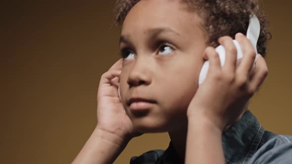 Little Boy Wearing Big Headphones and Nodding His Head on a Brown Background