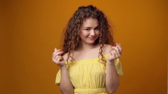 Young Woman Rubbing Fingers in Money Gesture Against Yellow Background