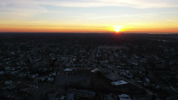 An aerial shot over a suburban neighborhood during a golden sunrise. The camera dolly out from the h alt