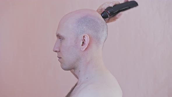 An Adult Bald Man Shaves His Head with an Electric Razor