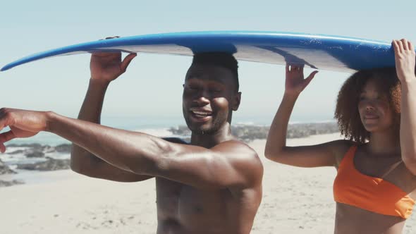 African American couple holding a surfboard on their heads alt