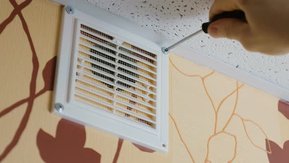 Male Hands Unscrew the Screws with a Screwdriver on the Grate Vents Home